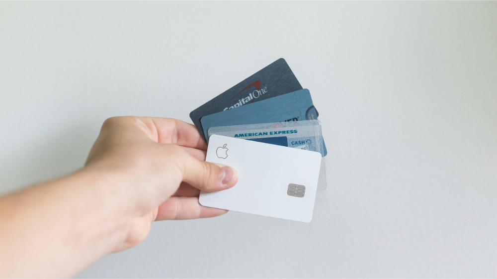Hand holding a fan of credit cards from various companies against a light background