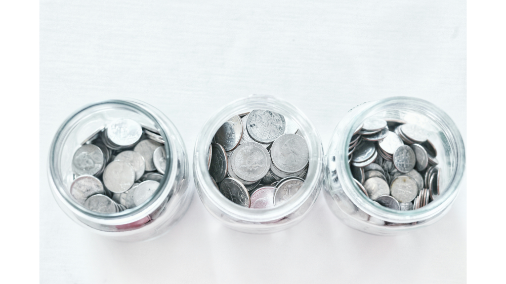 Three glass jars filled with assorted silver coins on a white background