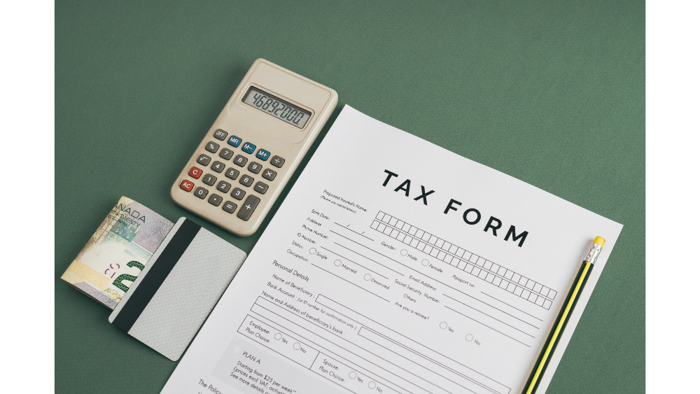 Flat lay of a tax form, calculator, credit card, and Canadian dollar bills on a green surface.