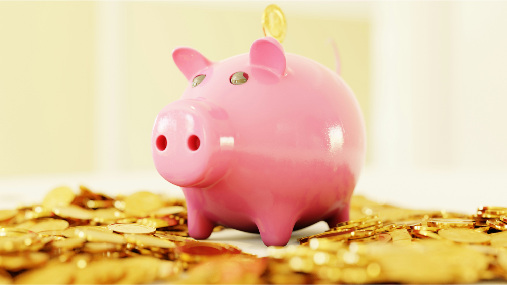 Pink piggy bank surrounded by gold coins with a single coin being inserted.