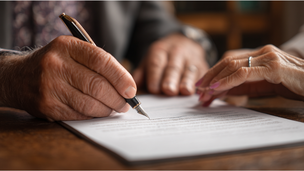 Close-up of elderly hands signing a legal document with a fountain pen on a wooden table