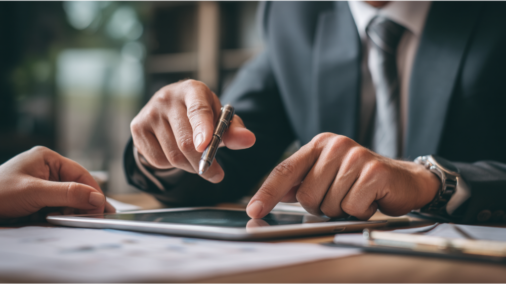 Close-up of a business professional in a suit pointing at a tablet screen during a client meeting