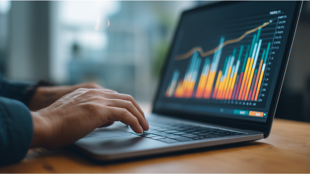 Close-up of hands typing on a laptop keyboard with a vibrant financial dashboard showing bar and line graphs on the screen.