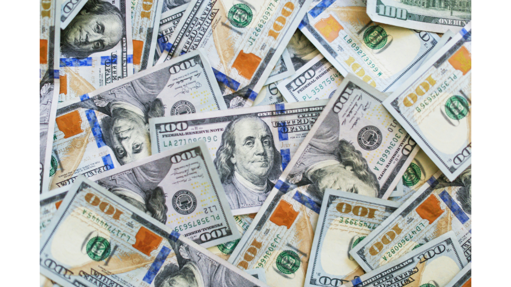 Scattered pile of U.S. one hundred dollar bills featuring Benjamin Franklin.