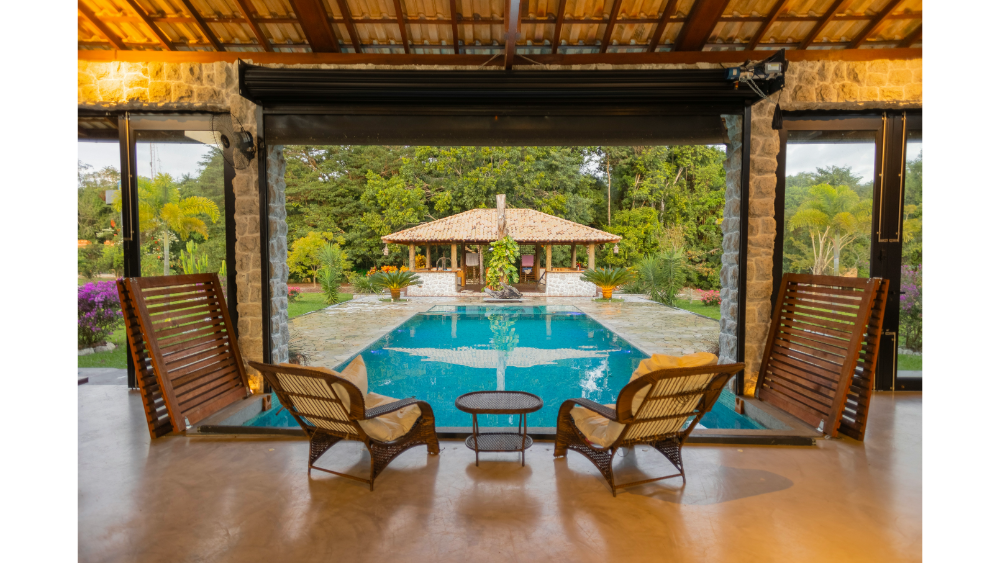 Cozy poolside seating area looking out onto a tranquil garden and stone pool house, surrounded by lush greenery.