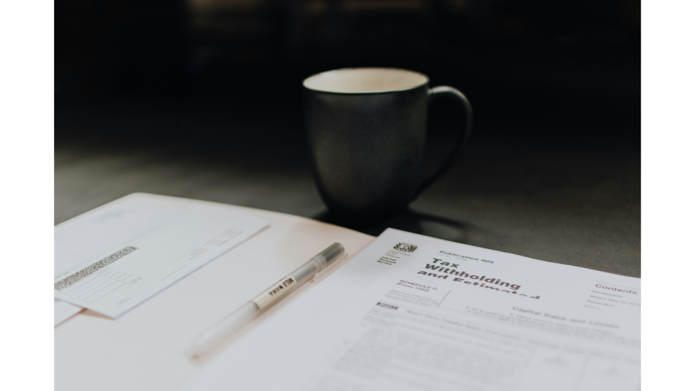Tax documents, a pen, and a coffee mug on a dark desk, symbolizing tax preparation or financial planning at home or in the office.