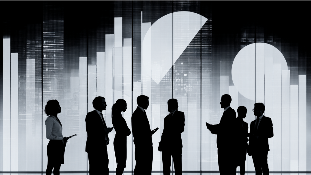 Silhouettes of businesspeople standing and talking in front of a screen displaying abstract charts and graphs.