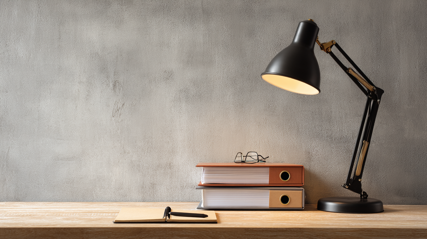 Desk with stacked binders, eyeglasses, a notebook, and a desk lamp.